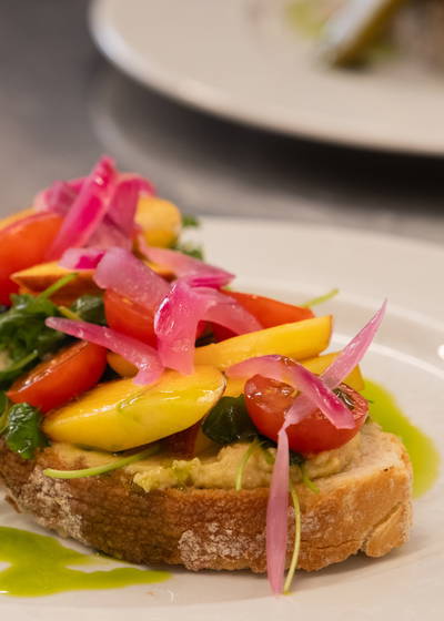 Vegetarsmørbrød på bruschetta pent pyntet med hummus, cherrytomater, nektarin, ruccola og syltet rødløk